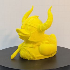 A yellow 3D printed duck in the style of a rubber ducky. This one is dressed as a barbarian, with a horned helmet and a giant axe.
