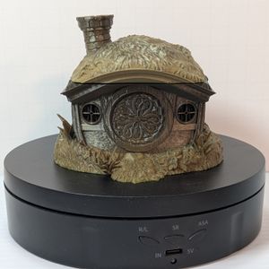 A 3D printed dice vault in the shape of the home of a halfling. It's got grass on the roof, a round chimney, and a round door. The top comes off to put the dice in. This one is a darker green gradient.