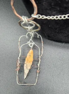 A close-up view of the hand-poured resin crystal with an orange- clear gradient and wrapped in a wire framework