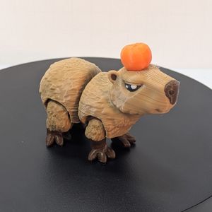 A smaller 3D printed Capybara, printed in a light brown filament for the coat and a lighter brown for the nose and feet. It's standing, and has articulation at the legs and mid-body. It has an orange Yuzu fruit on its head.