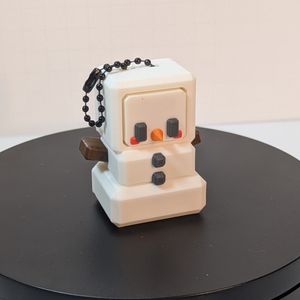 A 3D printed snowman. It's white, with brown "stick" arms, black "coal" eyes and buttons, red cheeks, and a pointy orange "carrot" nose. It's modeled very much like an 8 bit video game character, and it has a chain for hanging on its head.