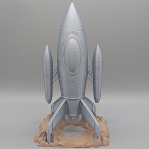 A silver retro-style rocket ship. It's shaped like a pointed cylinder, with two smaller pointed cylinders on the side. On the bottom around the rocket exhaust are four fins that rest in holes on the rock-like base.