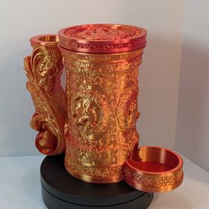A reddish-gold 3D printed tankard, with an ornate handle. The artwork on the side is of a dragon head, and there's a tray sticking out the bottom front to catch dice.