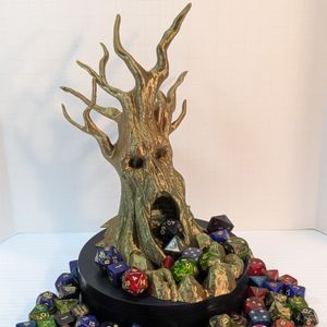 A 3D printed dice tower in the shape of a gnarled tree. Bare branches stick out the top, and the tree has a vaguely skull-like appearance, with hollow eyes, a missing nose, and the opening at the bottom looking like a screaming mouth.