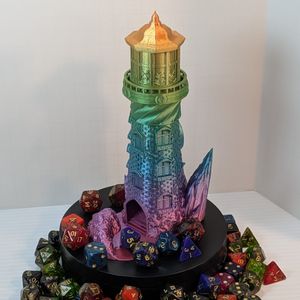 A 3D printed dice tower in the shape of a lighthouse, with a rocky base . It's printed in a very shiny rainbow filament. The dice catcher tray opens off to the side and it's surrounded by dice.