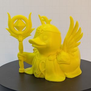 A 3D printed duck in the style of a rubber duck. It's printed all in yellow, and is dressed as a cleric, with a staff and wings.