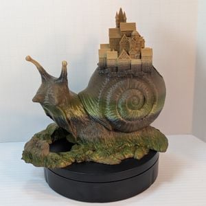 The front of the dice tower, showing the tray, and the green and brown gradient going up the tower, ending in a tan at the tips of the eye stalks and covering the town.
