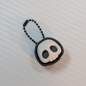 The 3D printed Skull clicker, with a ball link chain on top. It's a white skull with no lower jaw, with hollow black eyes. It's inside a black case that surrounds it and hides the keyboard switch, and gives the skull a black outline similar to a hood.