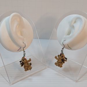A pair of 3D printed earrings, shaped like Jackalopes. They are light brown, with dark brown prongs, and they're attached to rainbow colored stainless steel earring hooks. They are hanging off the earlobes of silicone display ears.