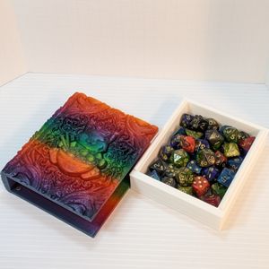 The happy ramen cat tome, with the pages removed from the box and resting beside it. The box is filled with TTRPG dice.