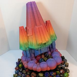A 3D printed dice tower in the shape of a space ship. The main body is a wedge, and the thrusters on either side are wedges. It's in a rainbow gradient filament, and the dice come out in the cloud of smoke under the thrusters. It's surrounded by dice.