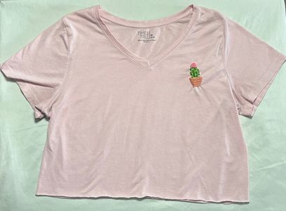 Pink shirt with cactus embroidery design on upper right hand side of shirt.