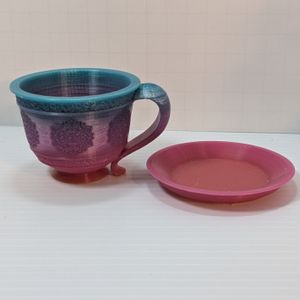 A 3D printed tea cup and saucer. It's printed out of a rainbow gradient filament, but due to its smaller stature, it is just from blue at the top to purple to red at the bottom, and the saucer is just reddish pink.