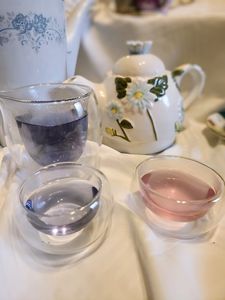 a photo of the two colors the tea can be in front of two floral teapots and a glass pitcher