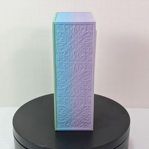 A rectangular 3d printed dice tower slash box. It's in a pastel rainbow gradient, going from green to light blue to pink. There is decorative work along the side.