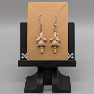 A pair of 3D printed mouse earrings, hanging on the brown card they will be shipped on.