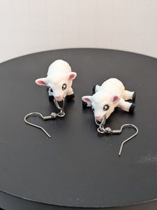 A pair of 3D printed earrings in the shape of lambs. One is standing on four legs looking at the camera, the other is laying on it's stomach with the legs splayed out at the sides. They both have silver earring hooks clasped in their mouths.