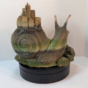 The back of the 3D printed Snail Town dice tower. It's in an earth-tone gradient, going from shades of browns to greens to tan, which mostly covers the town and the tips of the eye stalks.