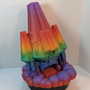A 3D printed dice tower in the shape of a space ship. The main body is a wedge, and the thrusters on either side are wedges. It's in a rainbow gradient filament, and the dice come out in the cloud of smoke under the thrusters.