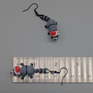 3D printed earrings of raccoons wearing Santa hats, with one laying on a ruler, showing a length with the earring hook of 2.5 inches.