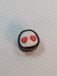 The 3D printed Heart Skull clicker, with no chain. It's a white skull with no lower jaw, with big red heart-shaped eyes. It's inside a black case that surrounds it and hides the keyboard switch, and gives the skull a black outline.