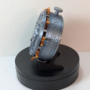 The side of the dice box. It's shaped like a large pocket watch, with knotwork on the side and gears and levers sticking out of the lid to change numbers on the counter. The box itself is a metallic silver, and the switches are bronze with black numbers.