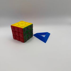 Turn it Tactile Speed Cube next to Turn it Tactile Cube Stand. The cube stand is triangular and has Turn it Tactile in print on one side and Turn it Tactile in braille on another.