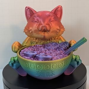 A 3D print of a happy looking cat, sitting behind a bowl of ramen. The cat is printed in a shiny rainbow gradient.
