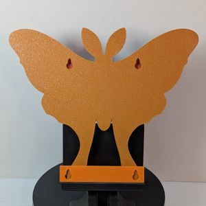 The back of the shelf. It's orange, and it has a pair of holes for screws to mount it on the wall. At the base of the shelf is an orange piece that is used as a spacer for the screws.