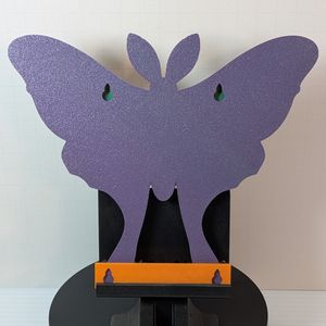 The back of the shelf. It's purple, and it has a pair of holes for screws to mount it on the wall. At the base of the shelf is an orange piece that is used as a spacer for the screws.
