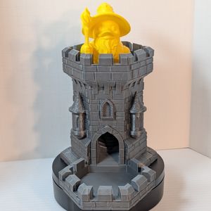 A 3D printed dice tower, shaped like a metallic steel castle tower. At the top is a yellow duck dressed as a wizard, holding a twisted staff.