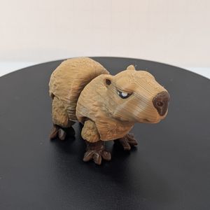 A smaller 3D printed Capybara, printed in a light brown filament for the coat and a lighter brown for the nose and feet. It's standing, and has articulation at the legs and mid-body.