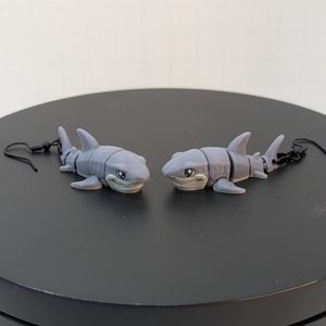 A pair of slightly cartoonish-looking 3D printed earrings, shaped like great white sharks. 