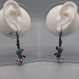 A pair of 3D printed earrings, in the shape of raccoons wearing Santa hats, hanging from a pair of fake white silicone display ears.