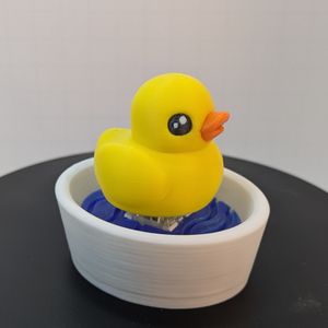 A 3D printed yellow ducky with an orange bill, on top of a small white bowl filled with blue "water." You can just barely see the mechanical keyboard switch between the duck and the water.