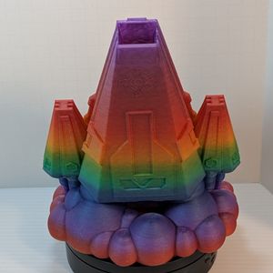 A 3D printed dice tower in the shape of a space ship. The main body is a wedge, and the thrusters on either side are wedges. It's in a rainbow gradient filament, and the dice go in the tip of the nose cone..
