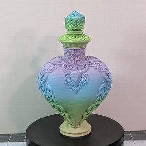 The 3D printed dice vault. It's a heart shaped bottle, with a lid that's capped with a d20. It's in a pastel rainbow, and there is scroll work around the edges and lid.