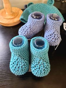 Two pairs of baby booties in size 12-months, in the colors Teal (12) and Blue (08) from the Acacia yarn swatch options. 