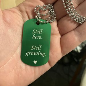 Hand holding a green laser engraved tag with attached necklace chain