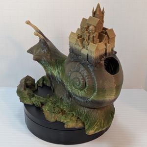 A slight rear shot of a 3D printed dice tower that looks like a snail with a town on its shell. This shows where the dice go into the shell under the town.