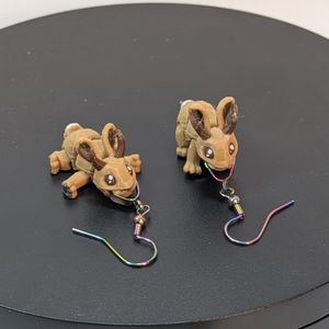 A pair of 3D printed earrings, shaped like Jackalopes. They are light brown, with dark brown prongs, and they're attached to rainbow colored stainless steel earring hooks.