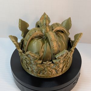 A 3D printed dice vault in the shape of a crown. It's printed in a brass colored filament.