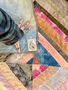 A close up of Polychrome withe the corner turned back to show the flame & honeycomb tag and the name hand embroidered with undyed organic cotton thread