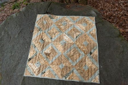 The Honey Bee Quilt laying flat on a large rock in the forest