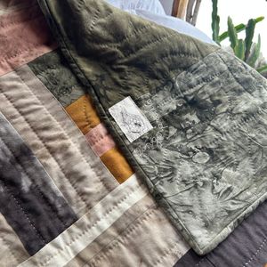 A corner of Fingerprints folded back to show the flame & honeycomb label along with the name hand embroidered in undyed organic cotton thread