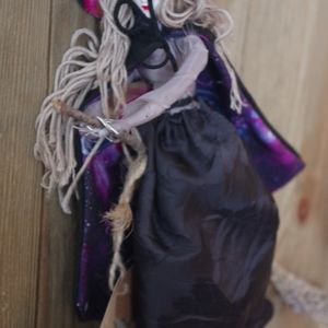 Image of handmade doll named Lavender wearing a witch's hat and cape with a space themed lining and riding a broom made of lavender.