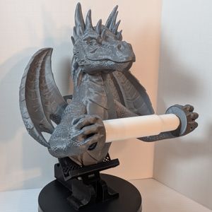 A 3D printed toilet paper holder in the shape of a dragon. It's a dull Steel color, and its front claws are holding the spindle for the toilet paper roll out away from its chest.