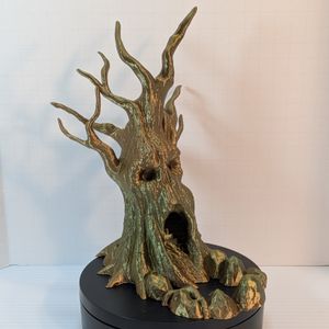A 3D printed dice tower in the shape of a gnarled tree. Bare branches stick out the top, and the tree has a vaguely skull-like appearance, with hollow eyes, a missing nose, and the opening at the bottom looking like a screaming mouth