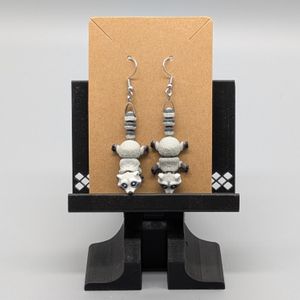 A pair of raccoon earrings 3D printed in color. They are displayed on the brown card they ship on.