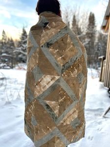 A photo of me from the back with the Honey Bee Quilt wrapped around me, standing in a winters landscape 